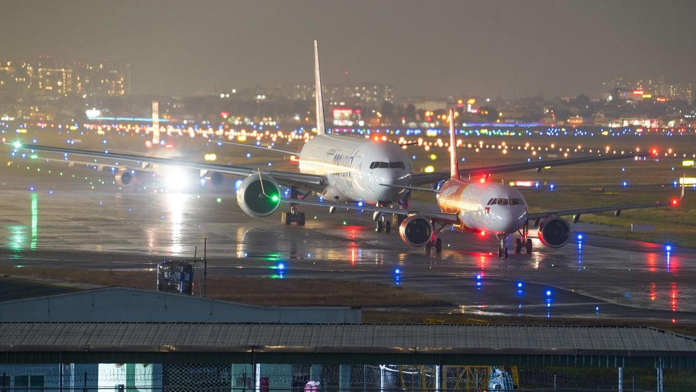 Multiple airplanes on a brightly lit runway at night with city lights in the background