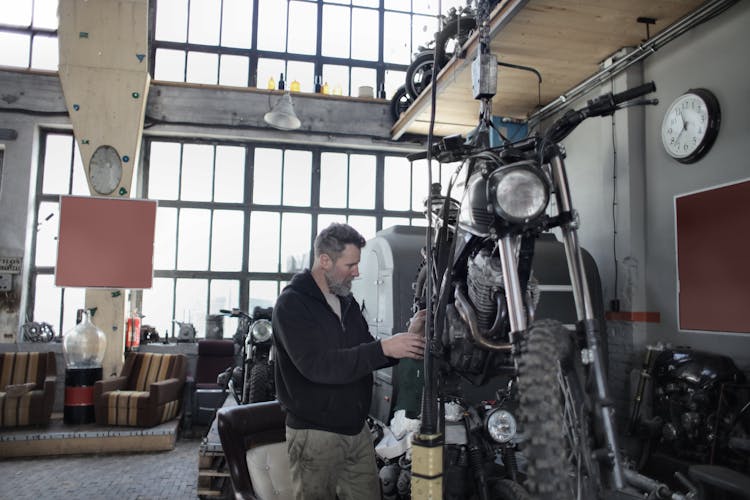 Bearded Mechanic Examining Motorbike In Garage