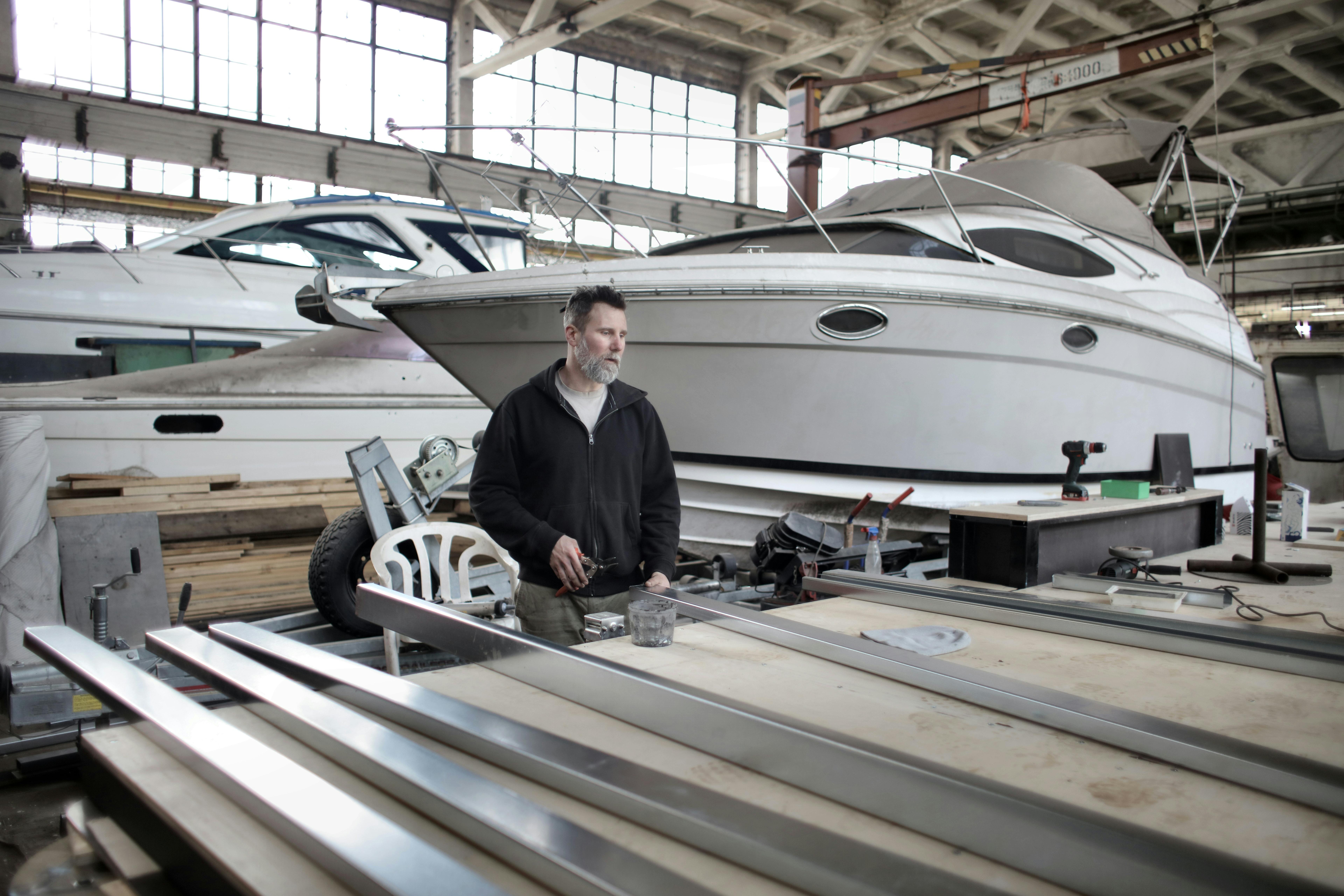 focused adult worker preparing metal details in workshop with yachts