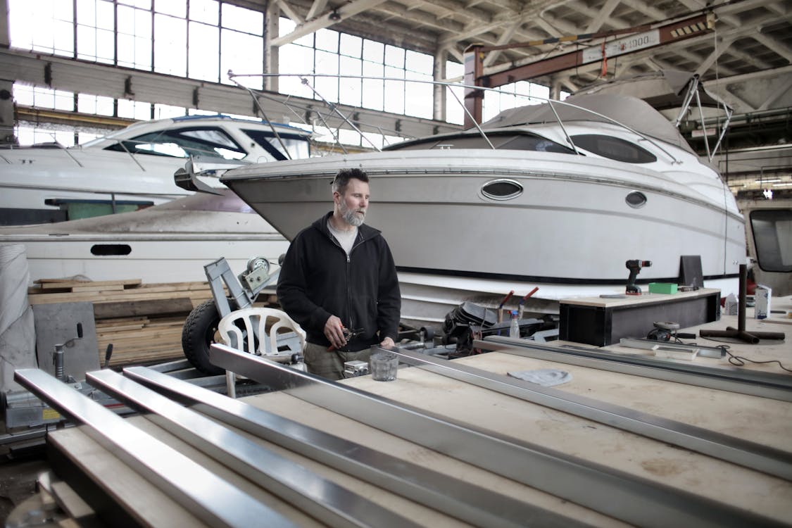 Focused adult worker preparing metal details in workshop with yachts