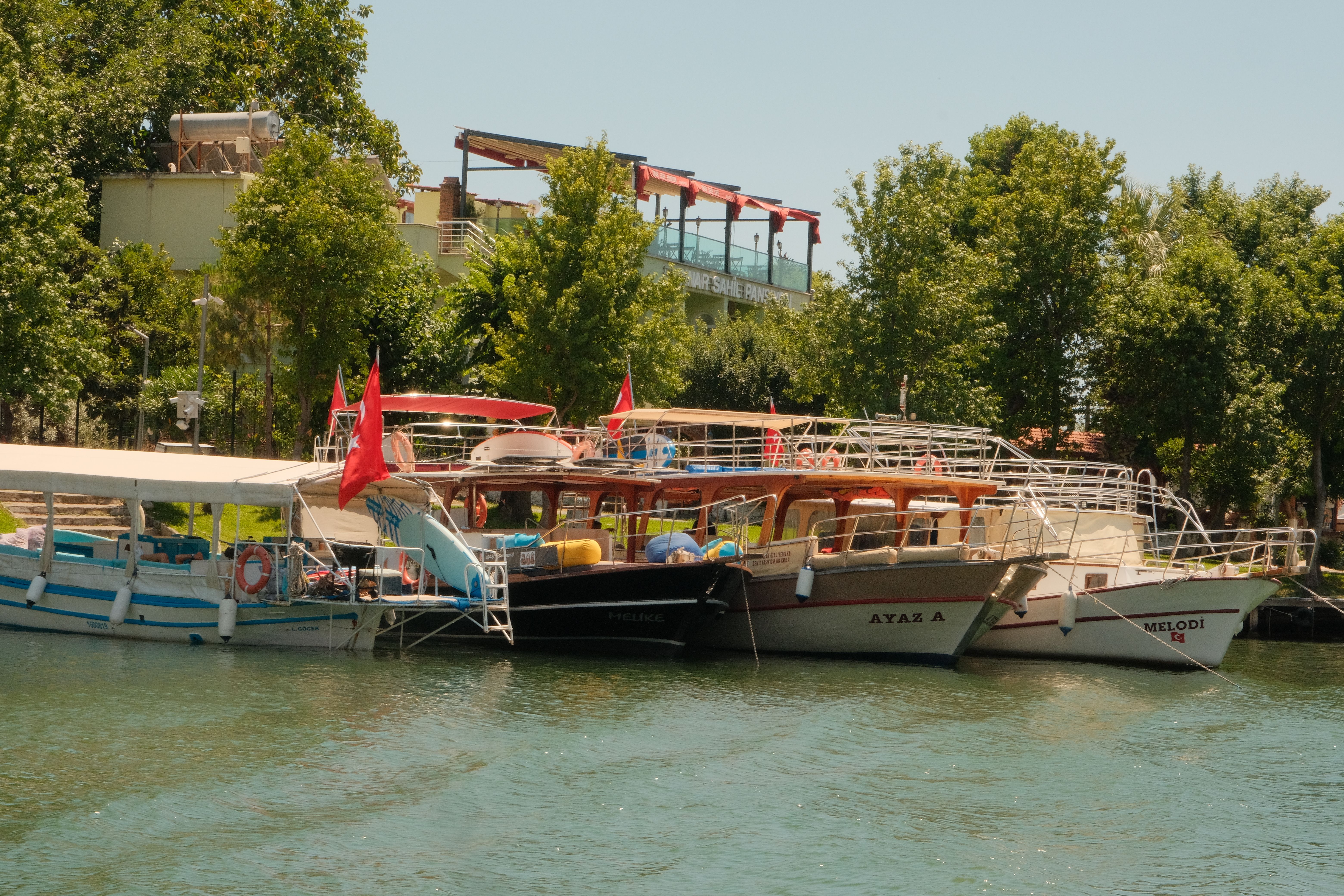 Charming scene of boats moored on the calm Dalaman River, surrounded by lush greenery.