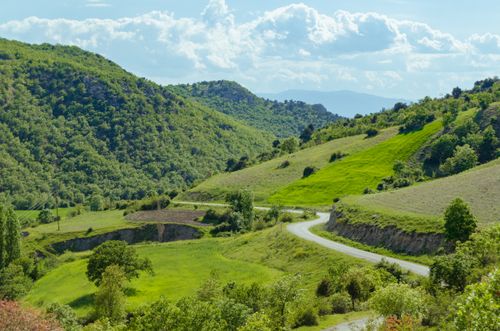 Free Beautiful green countryside landscape featuring a winding road and lush hills under a cloudy sky. Stock Photo
