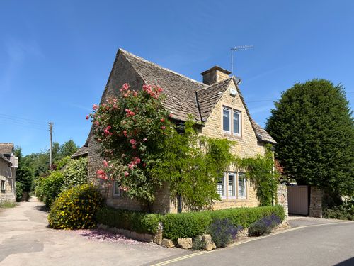 Free Idyllic stone cottage in the Cotswolds surrounded by vibrant flowers on a sunny day. Stock Photo