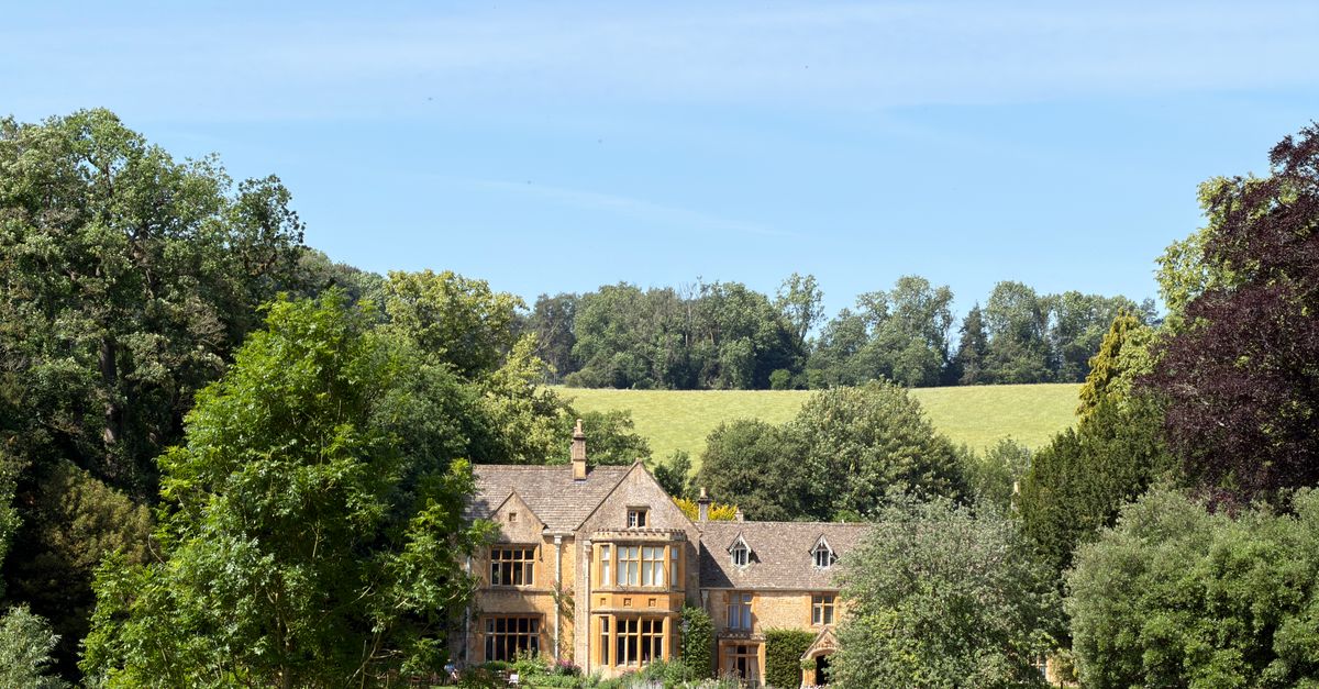 A picturesque historic manor surrounded by lush greenery in the English countryside during summer.