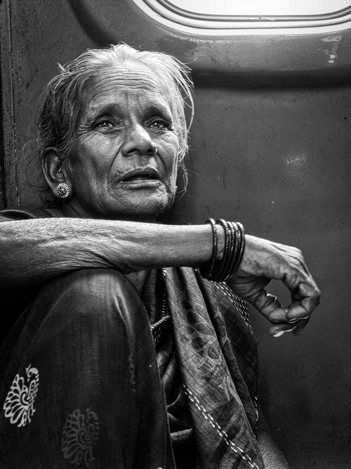 Free Monochrome portrait of an elderly Indian woman sitting in a train, lost in thought. Stock Photo