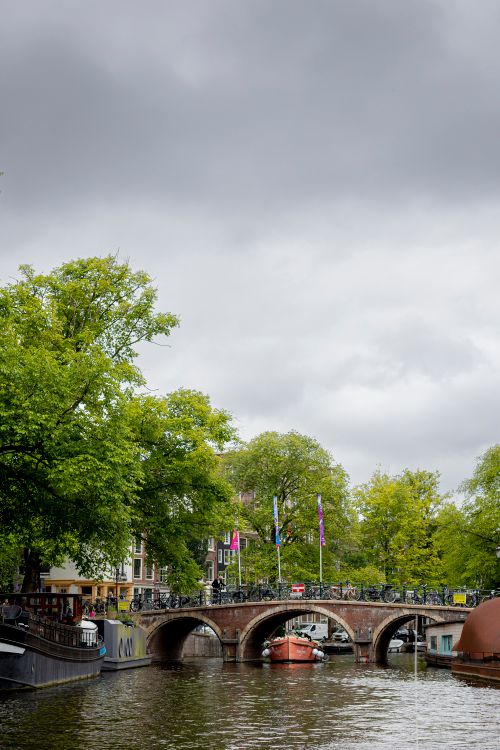 Free A picturesque view of Amsterdam's canals featuring a historic brick bridge under cloudy skies. Stock Photo