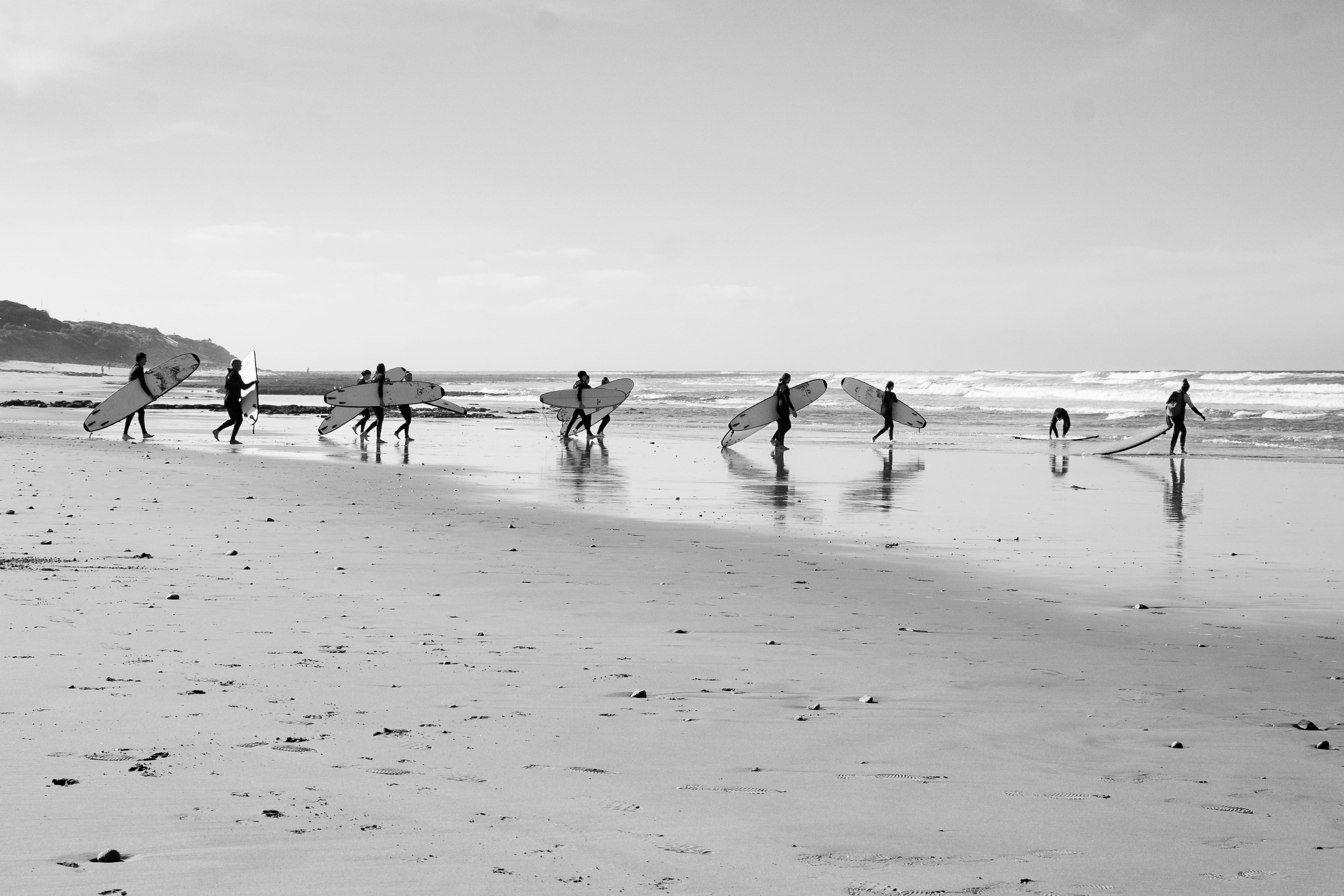 A group of surfers walking with boards on a tranquil beach, ready to catch the waves.