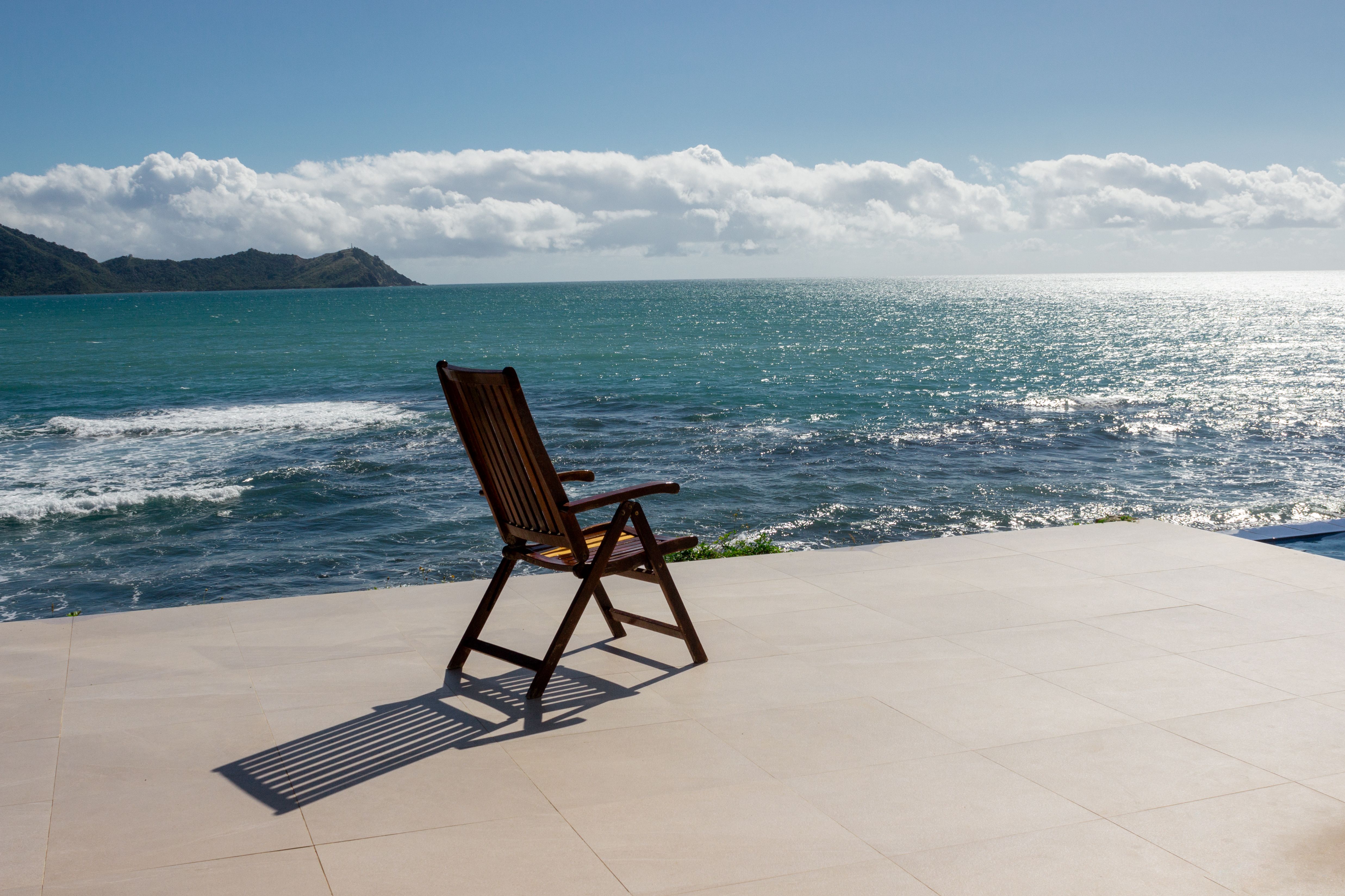 An empty wooden deck chair facing the serene ocean under a clear sky, ideal for relaxation themes.