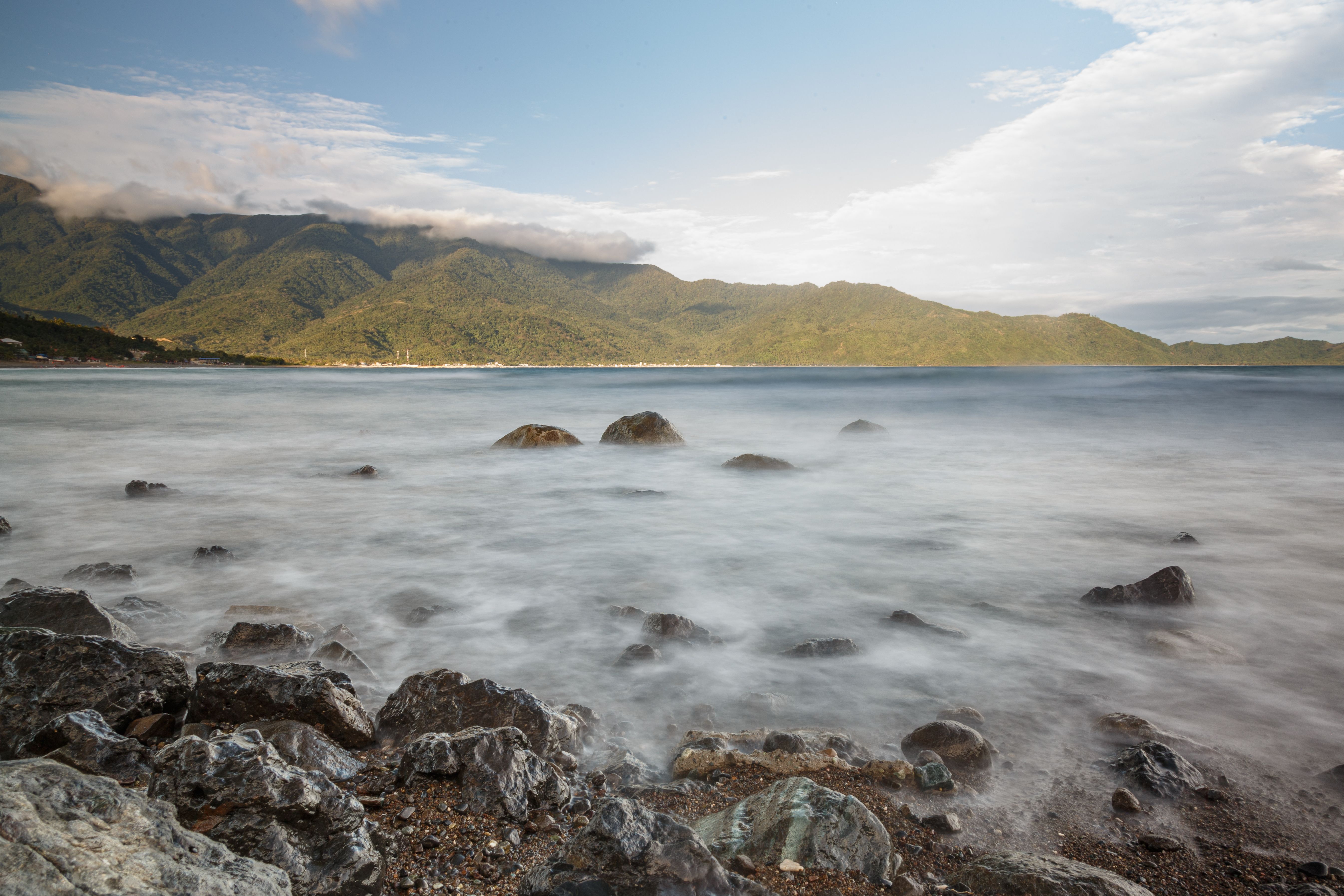 Peaceful ocean scene with a misty effect over rocks and distant green mountains.