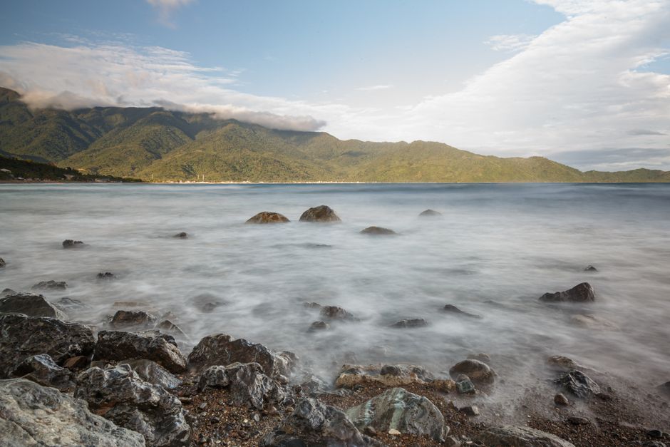 Peaceful ocean scene with a misty effect over rocks and distant green mountains.