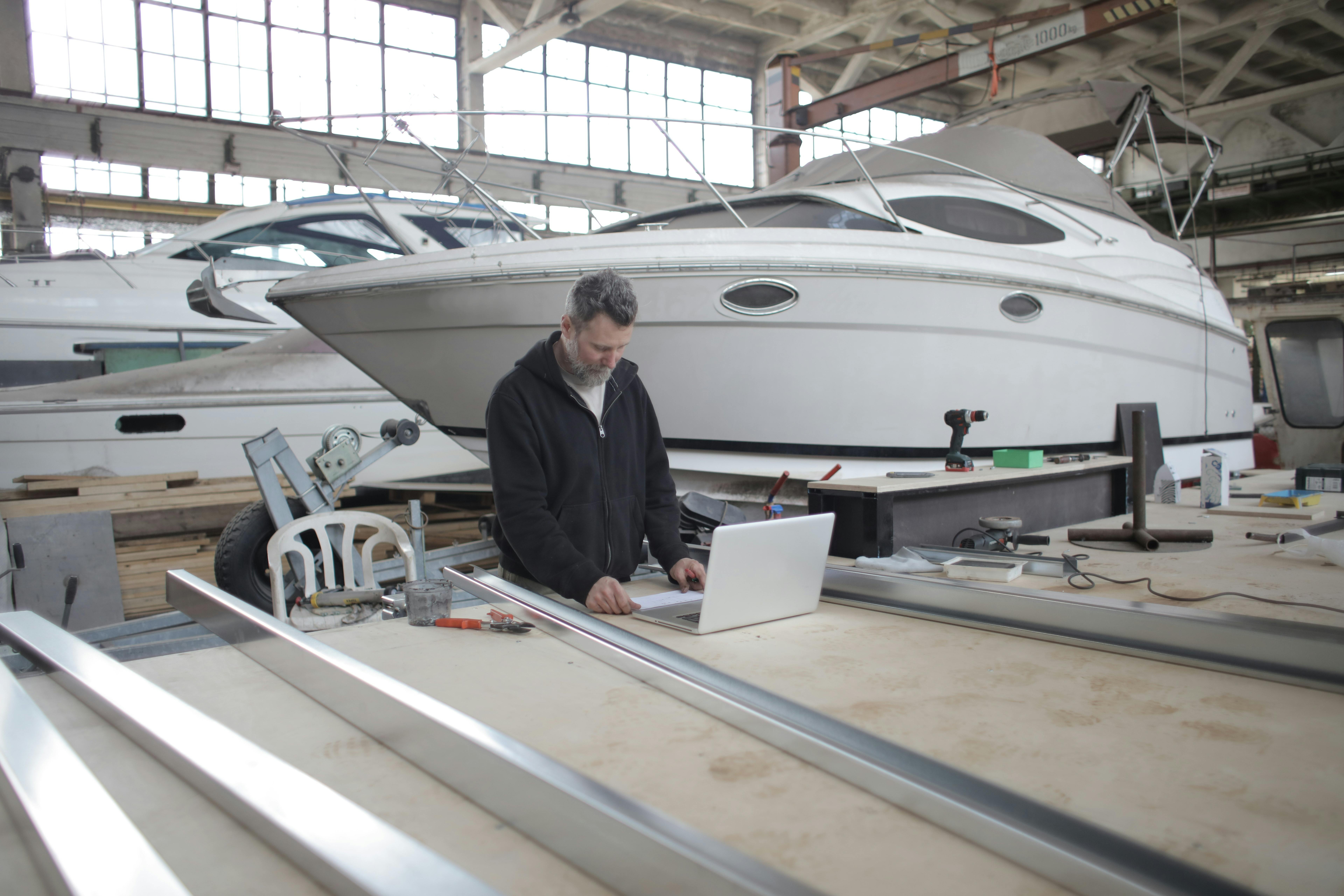 adult worker using laptop at workbench during work in boat garage