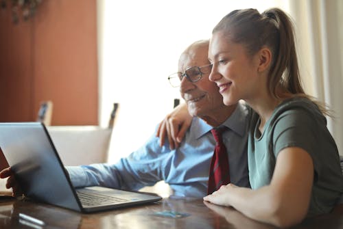 Young positive woman helping senior man using laptop