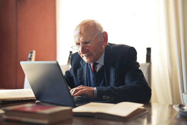 Serious Senior Man In Formal Suit Working On Laptop At Workplace