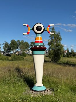 Vivid abstract sculpture in a grassy field under bright blue skies in Denmark.