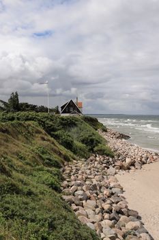 Idyllic beach house overlooking the rocky coast of Denmark beneath a cloudy sky.