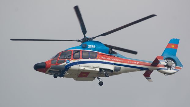 A vibrant Vietnam helicopter flying mid-air with a cloudy sky backdrop.