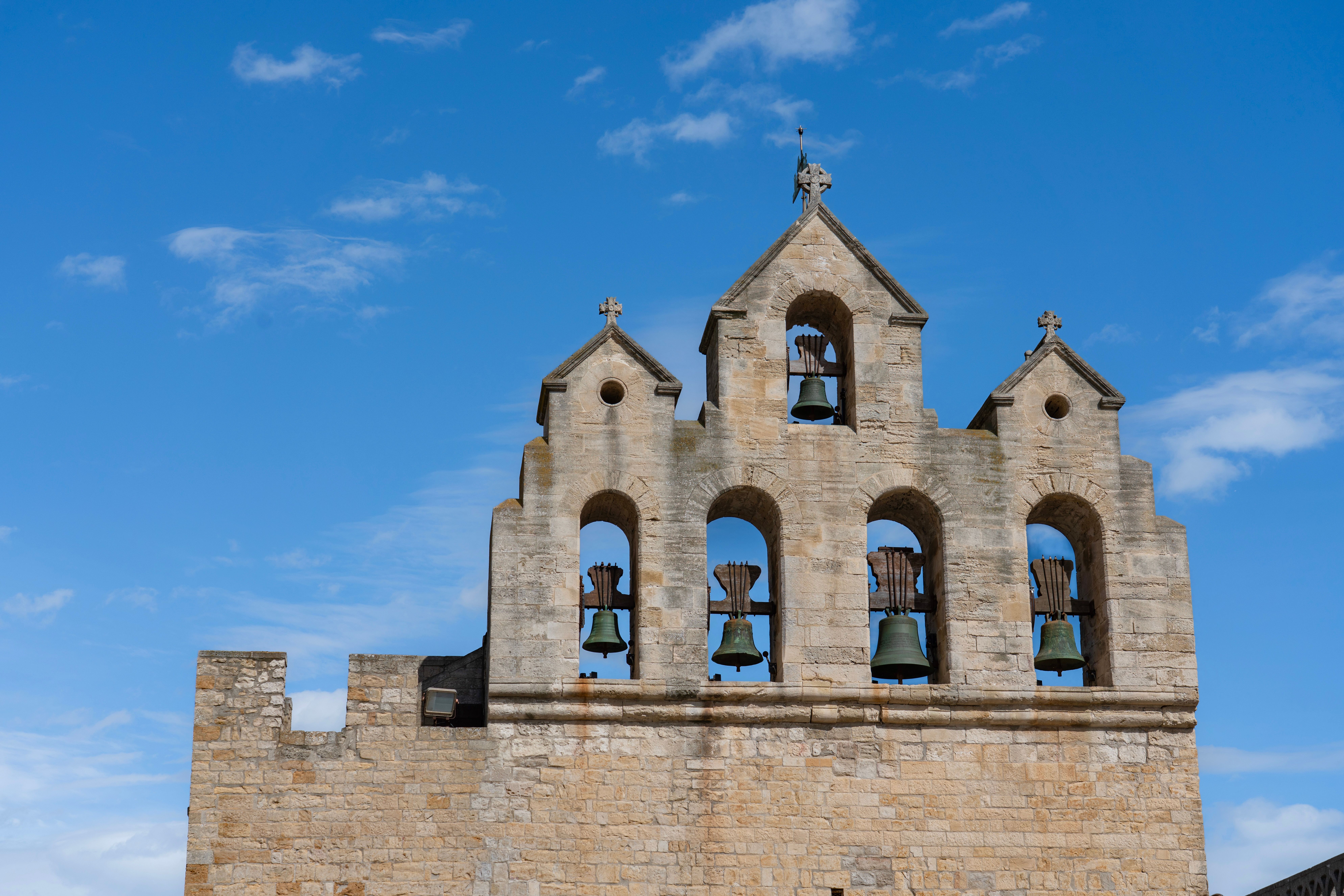 Ancient stone bell tower with five bells set against a clear blue sky, showcasing historical architecture.