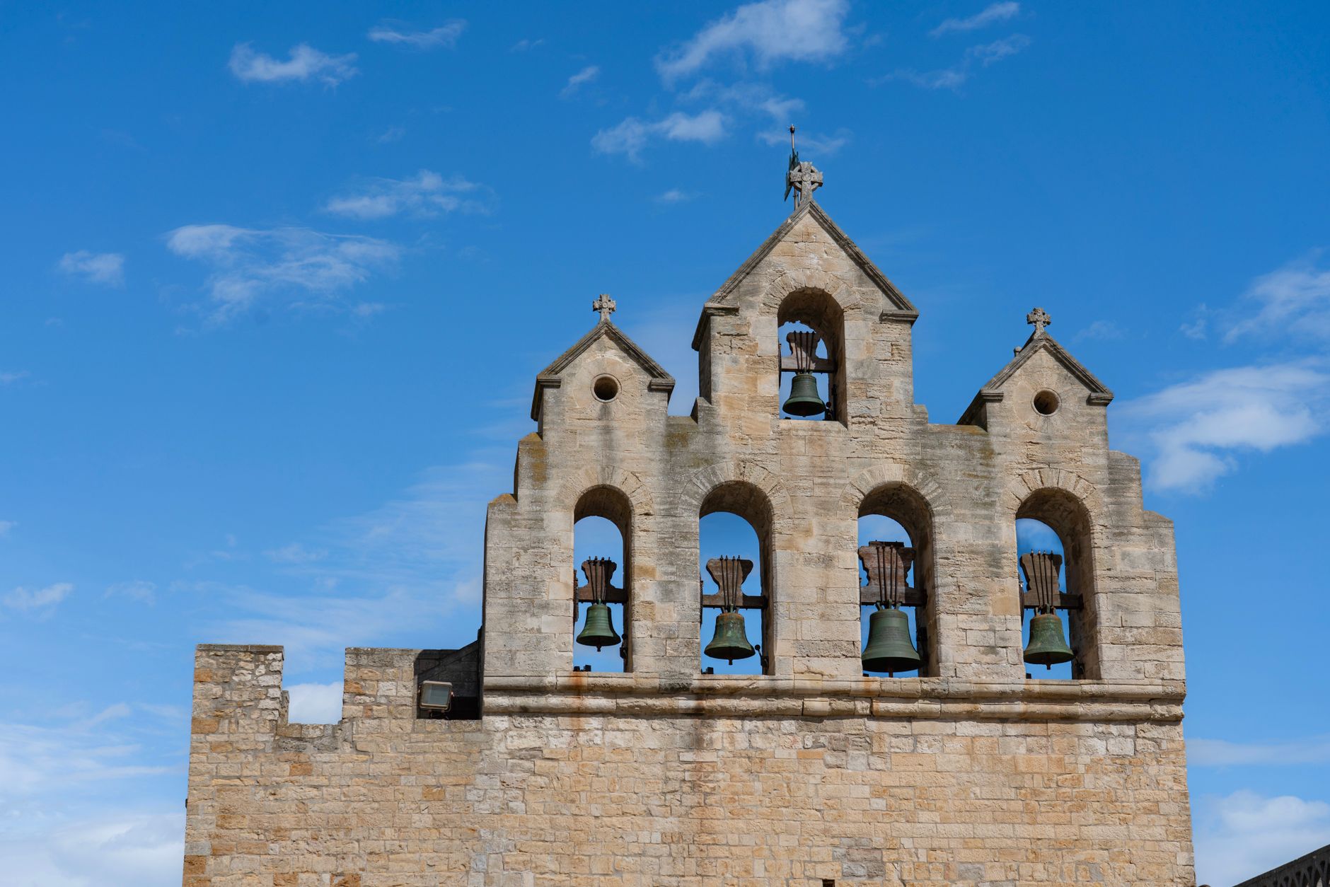 Ancient stone bell tower with five bells set against a clear blue sky, showcasing historical architecture.