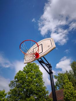 A basketball hoop photographed from below with a clear blue sky and scattered clouds, perfect for sports and outdoor themes.