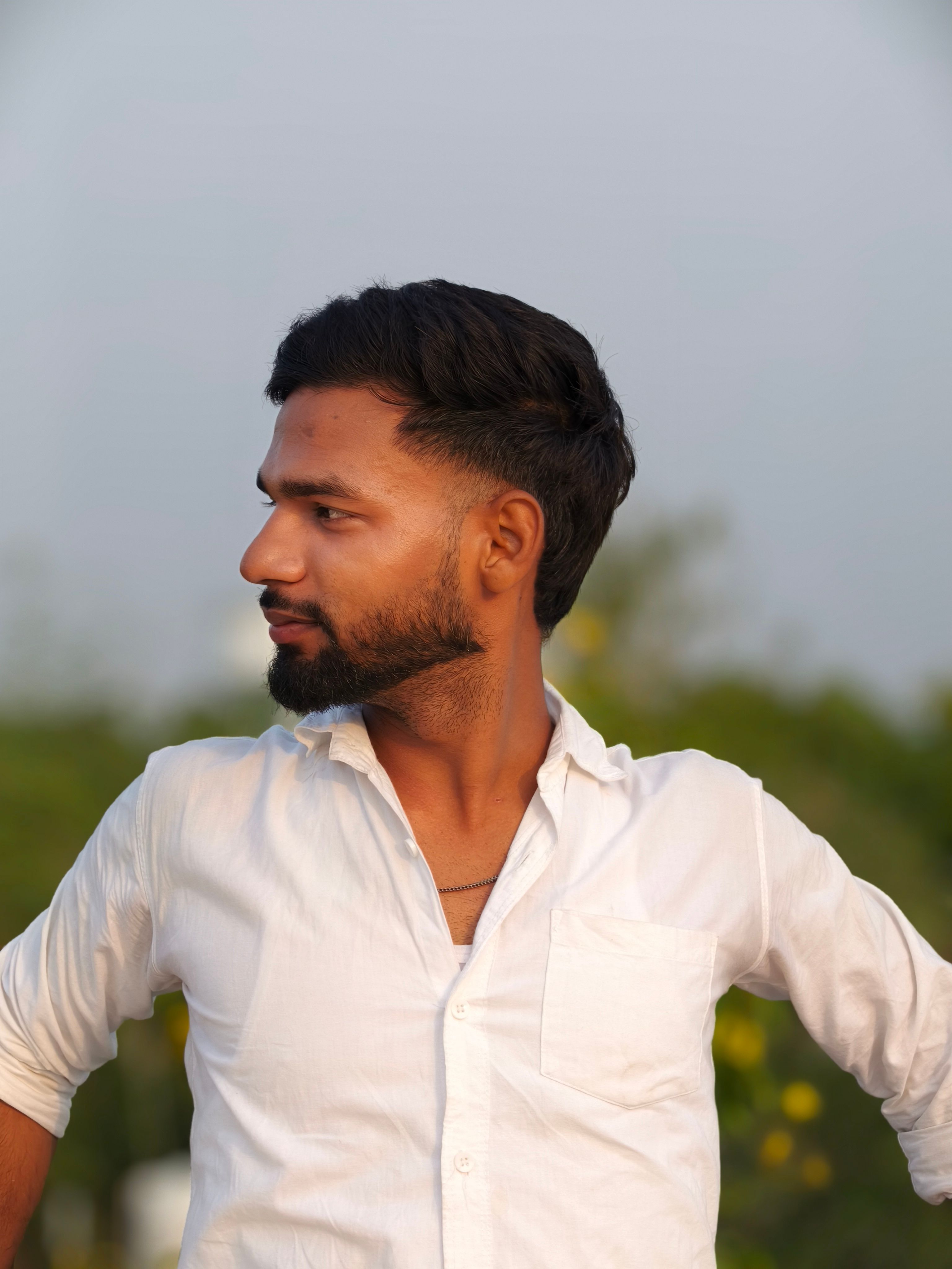 Side profile portrait of a man wearing a white shirt outdoors against a natural backdrop.