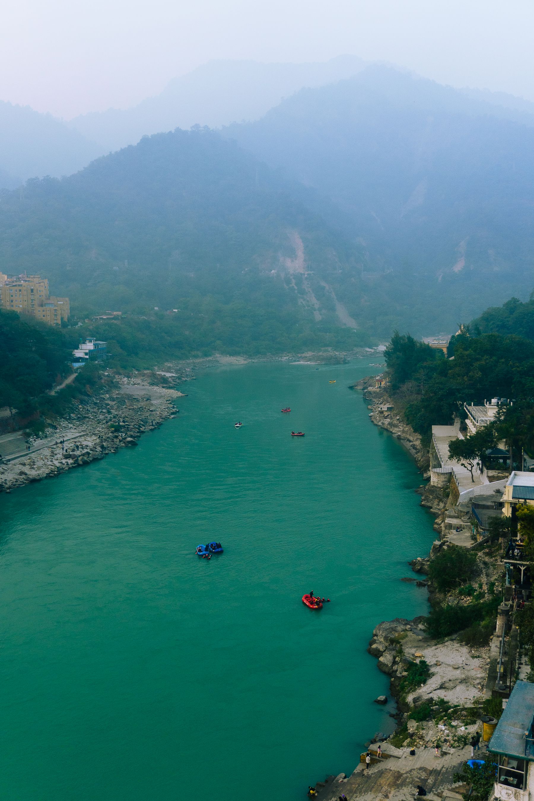 The Ganges running fast and green between forested hills at Rishikesh