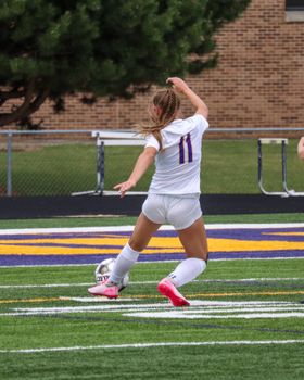 Vibrant shot of a female soccer player kicking a ball on an outdoor field during a match.