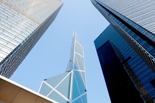 Dynamic upward view of iconic Hong Kong skyscrapers against clear blue sky.