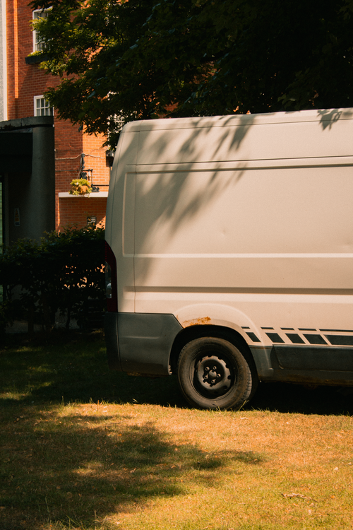 Free A white van parked outdoors under tree shade in a sunny Shrewsbury park. Stock Photo