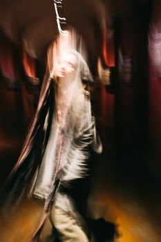 Artistic motion blur of a person walking in a dimly lit hallway with dramatic lighting.