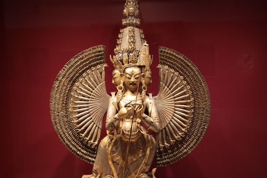 Detailed golden Buddhist statue with intricate design displayed in a museum.
