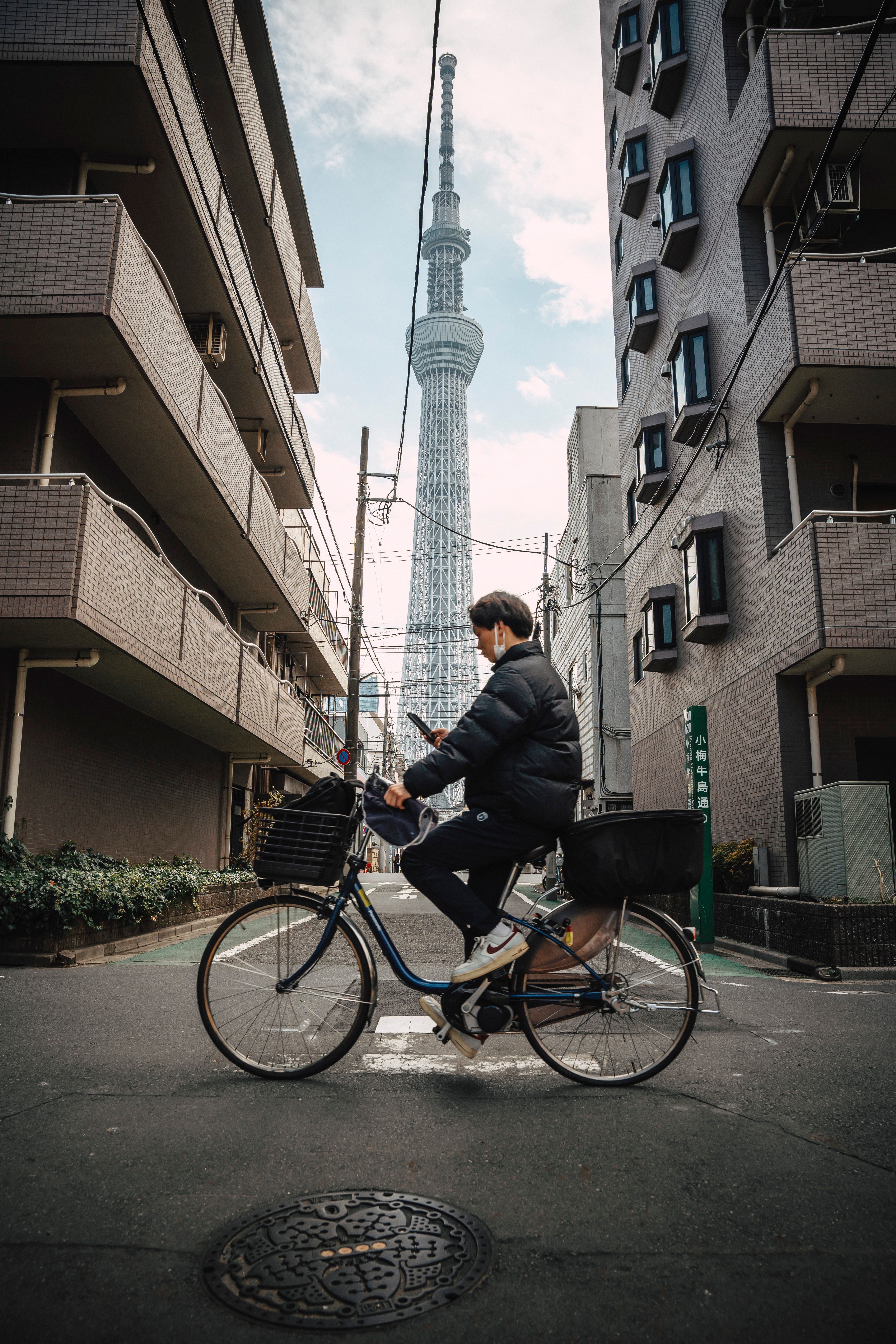 Man on bicycle with Tokyo Skytree in the background on a city street.