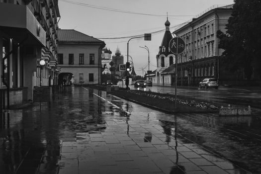 Monochrome urban street with wet pavement reflecting buildings after rain.