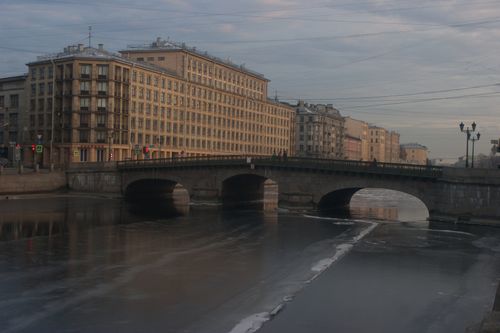 Free A historic stone bridge crossing a partially frozen river under a cloudy sky at dusk. Stock Photo