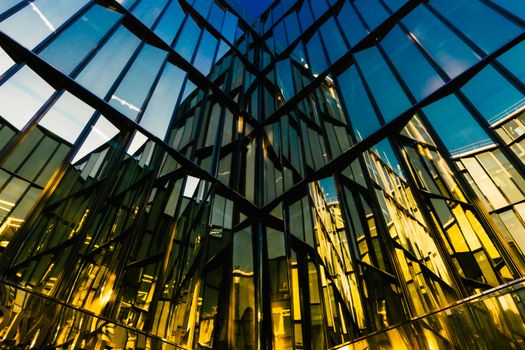 Modern building reflecting sky in abstract mirrored facade, showing golden hues.