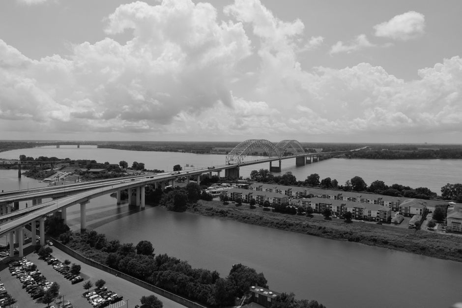Dramatic aerial view of the Hernando de Soto Bridge in Memphis, Tennessee, against a backdrop of clouds.