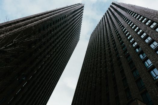 Two tall skyscrapers stretch upwards against a cloudy sky, showcasing modern urban architecture.