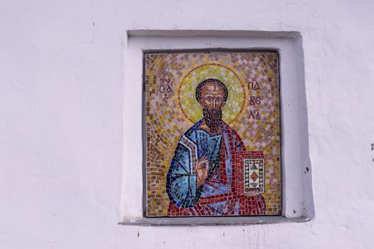 Colorful mosaic depicting a saint embedded in a white wall.