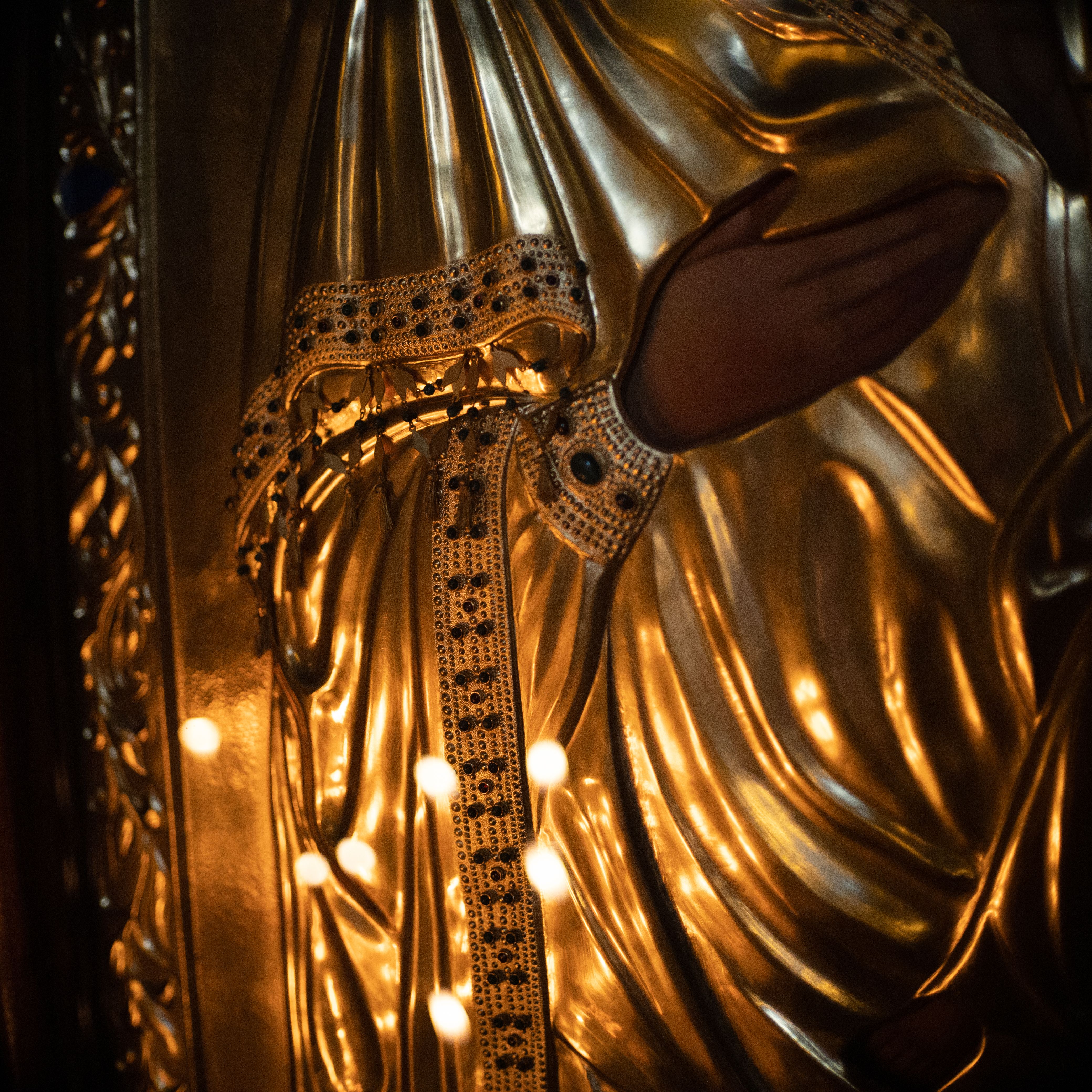 Detailed close-up of a golden religious statue with intricate embroidery and illuminated details.