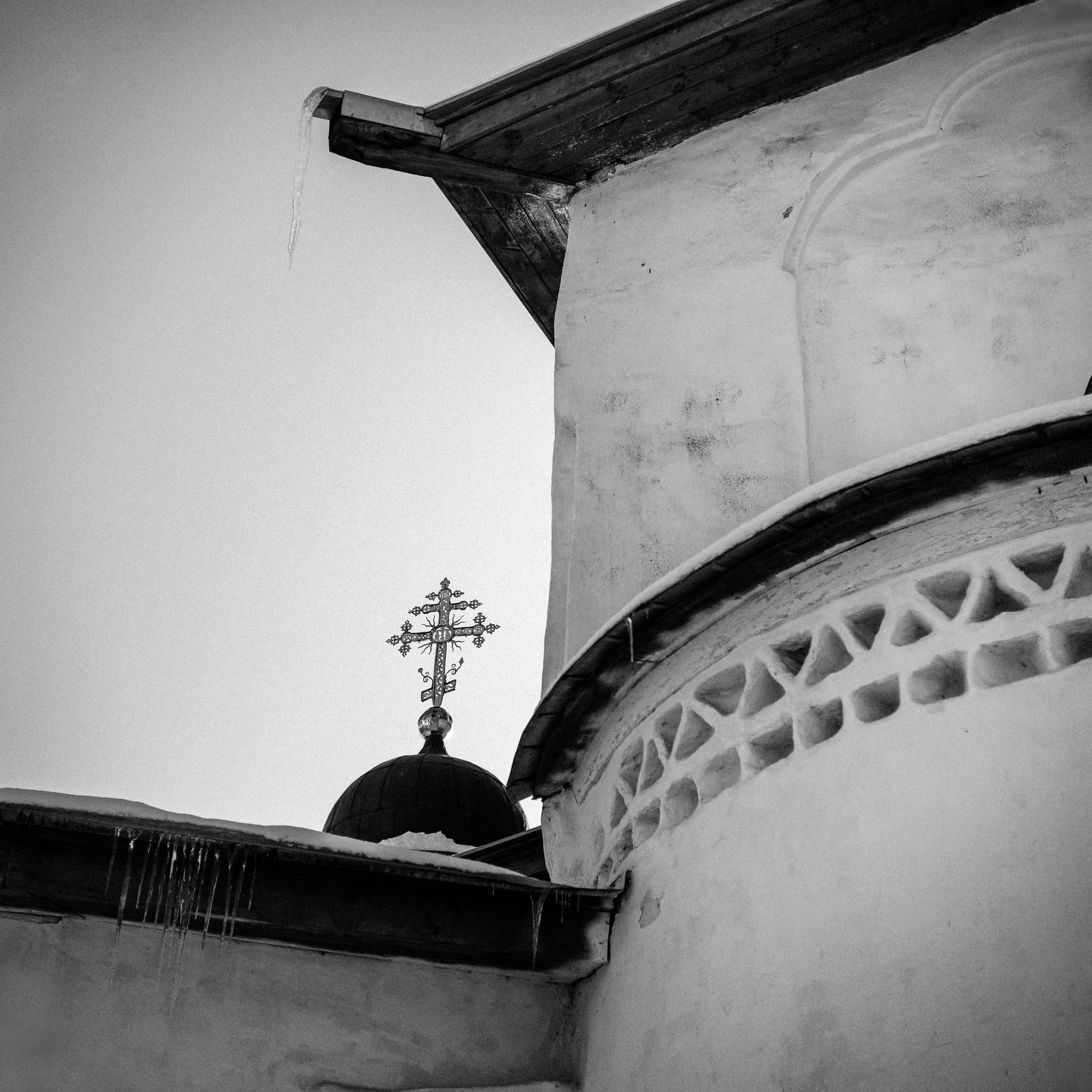 A wintry scene of an Orthodox church dome and cross in black and white, showcasing architectural details.