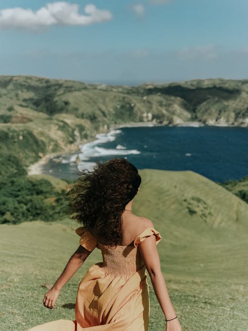 Женщина в коричневом платье без рукавов стоит на поле зеленой травы