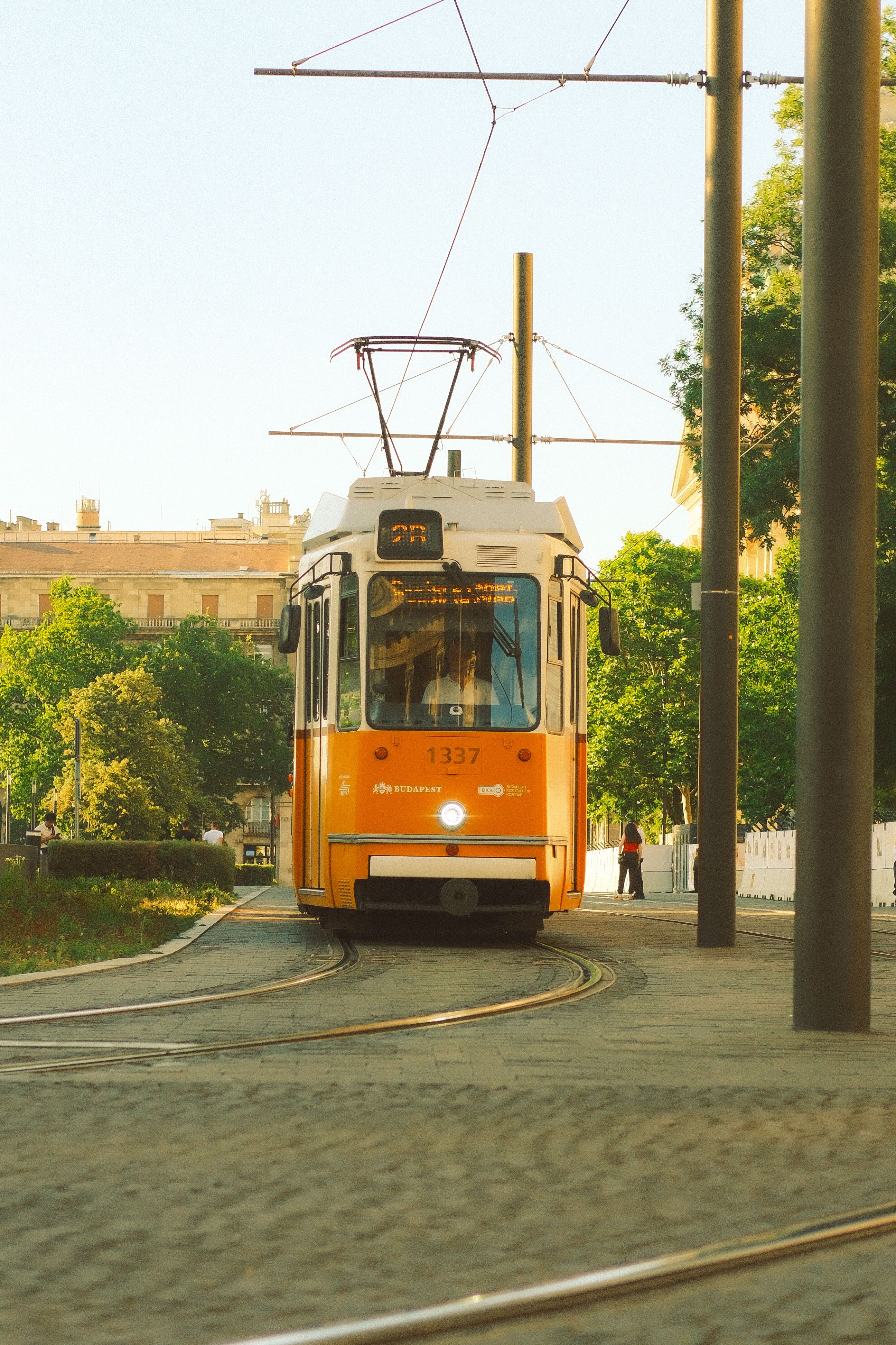 An iconic yellow tram navigating through Budapest in the summer, under clear skies.
