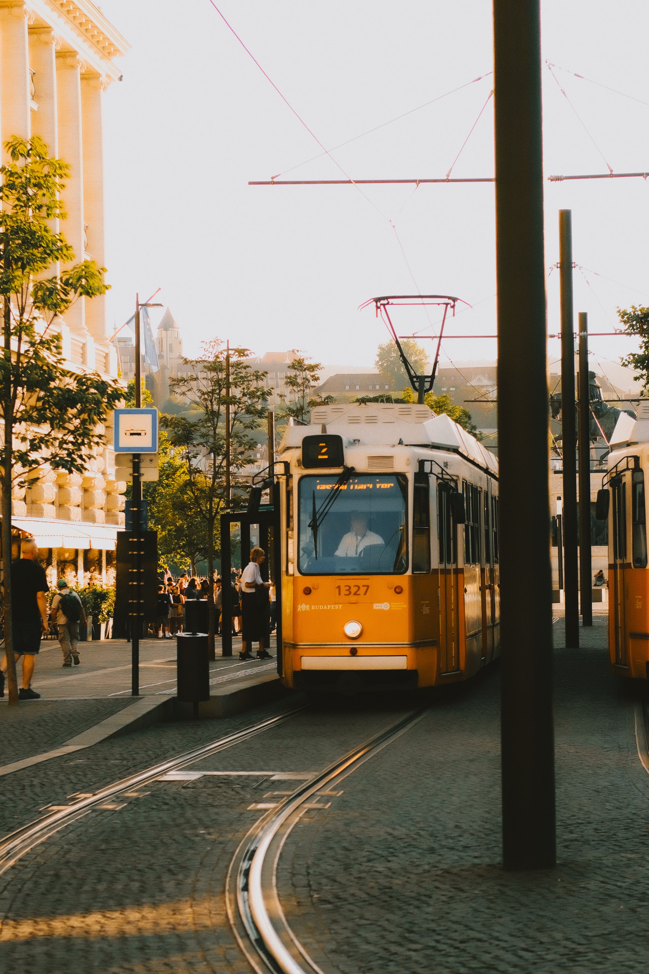 Yellow tram on a sunny street in Budapest, Hungary, showcasing vibrant city life and historic architecture.