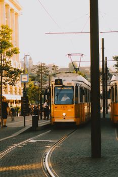 Yellow tram on a sunny street in Budapest, Hungary, showcasing vibrant city life and historic architecture.