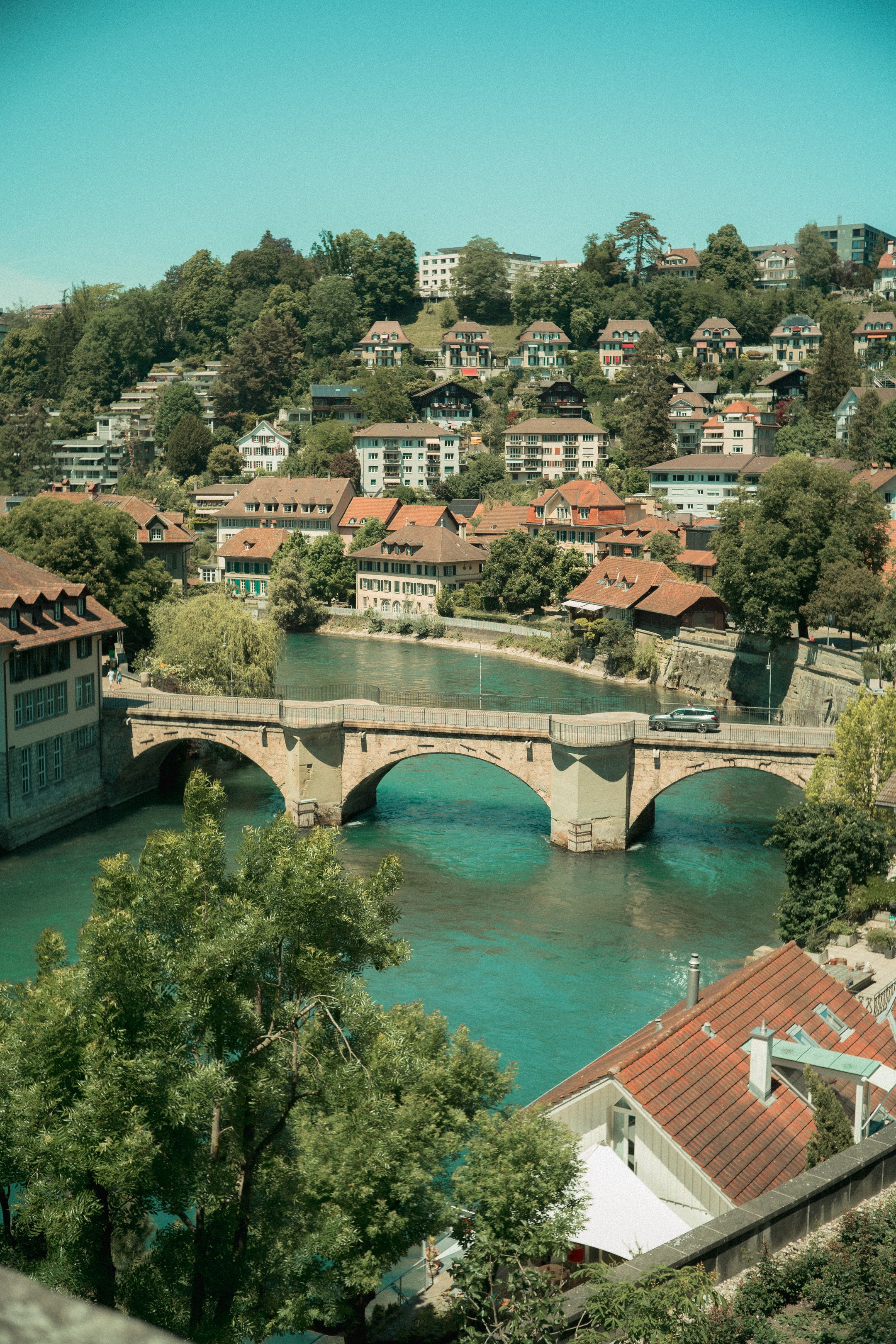 Picturesque view of a historic bridge over a turquoise river in a charming European town surrounded by lush hills.