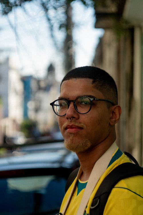 Free A young adult with glasses and a backpack stands outdoors in casual attire. Stock Photo