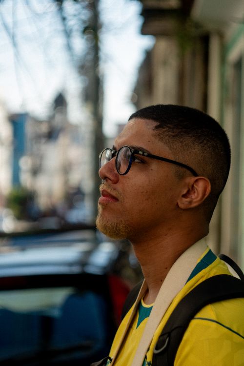 Free Portrait of a young man in glasses and sports jersey, standing on a city street. Stock Photo