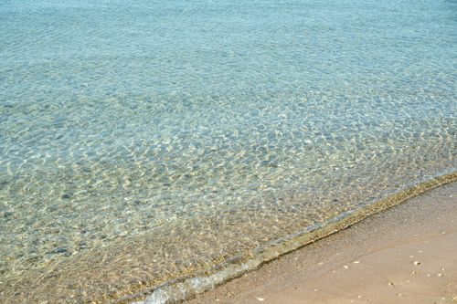 Free Tranquil scene of clear turquoise waters gently meeting the sandy shore at Yévre Beach. Stock Photo