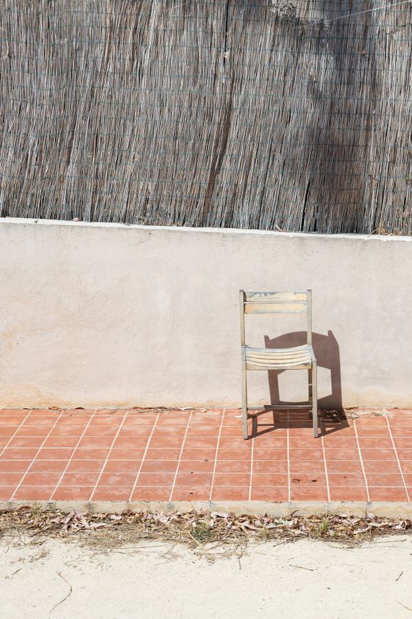 A rustic chair casting a long shadow on terracotta tile — photo by Bingqian Li on Pexels