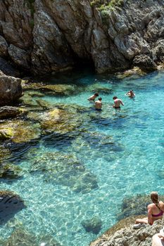 A serene scene of people swimming and relaxing in the clear waters near rocky cliffs in France.