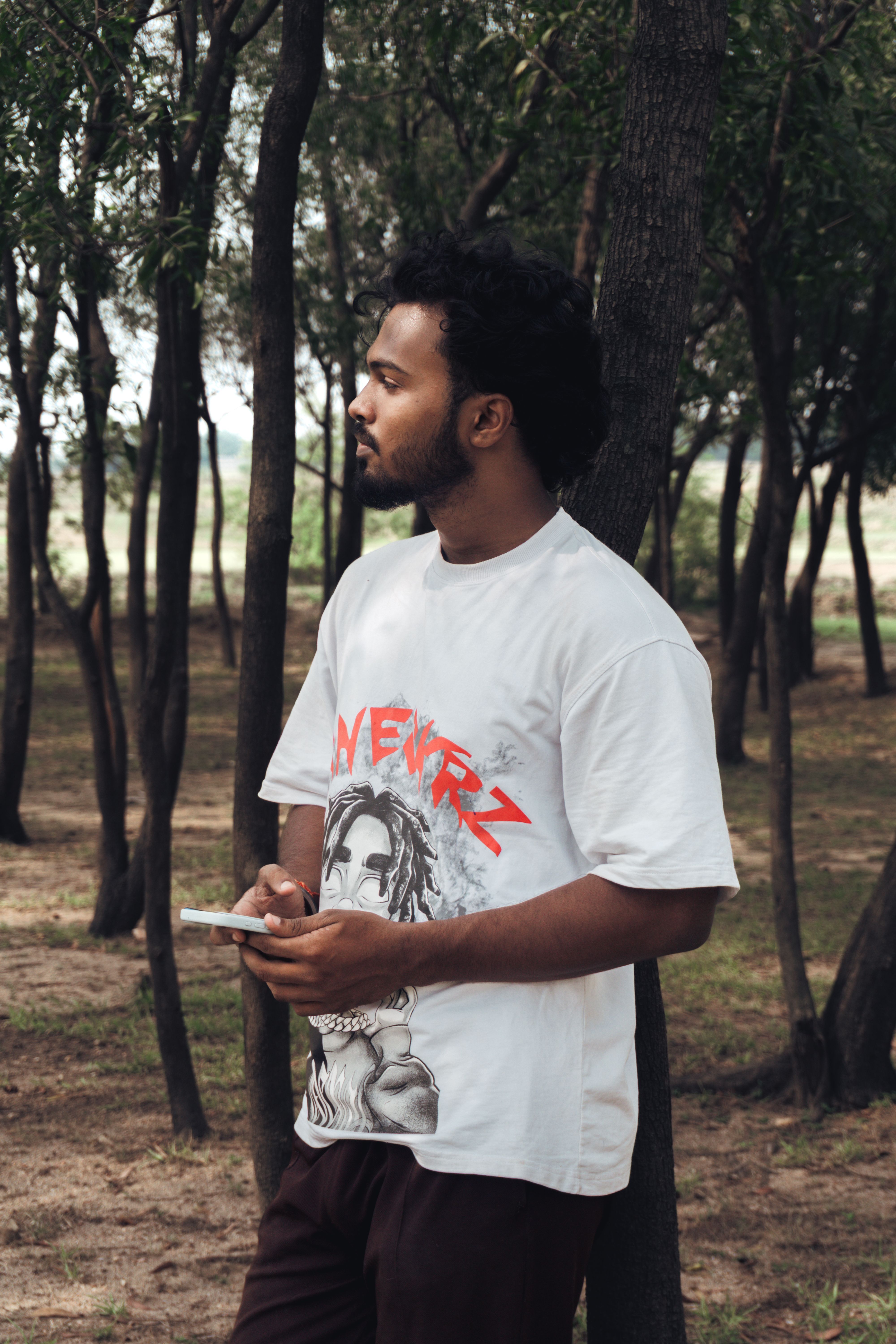 Young man standing in forest using a smartphone, wearing graphic t-shirt.